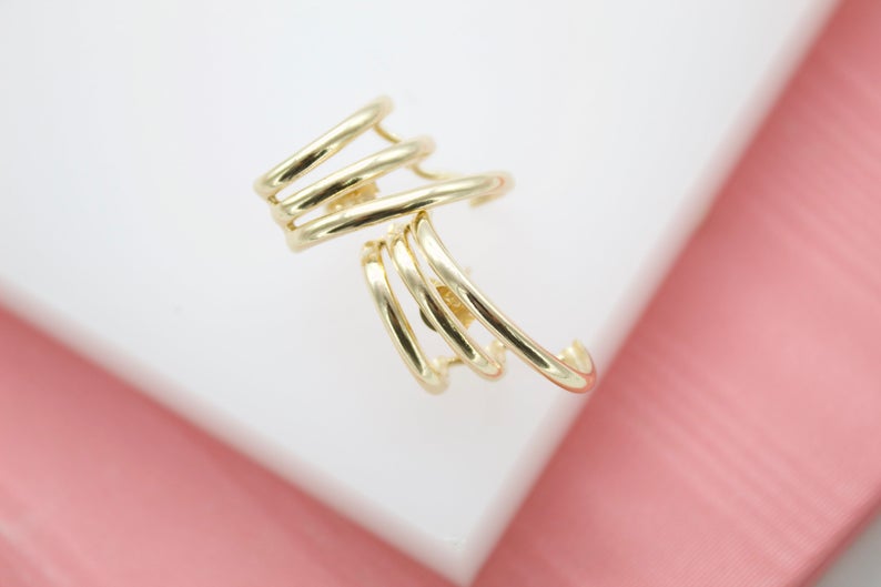 A modern gold multi-band ear cuff rests on a white and pink display surface.