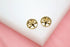 Two gold tree of life stud earrings rest on a white display block against a soft pink background.