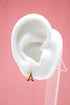 A white mannequin ear displays a gold and red Eiffel Tower stud earring against a pink background.
