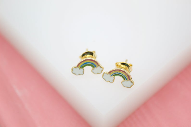 A pair of gold rainbow and white cloud stud earrings rests on a white surface.