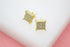A pair of gold square stud earrings encrusted with sparkling micro pavé stones rests on a white display surface.