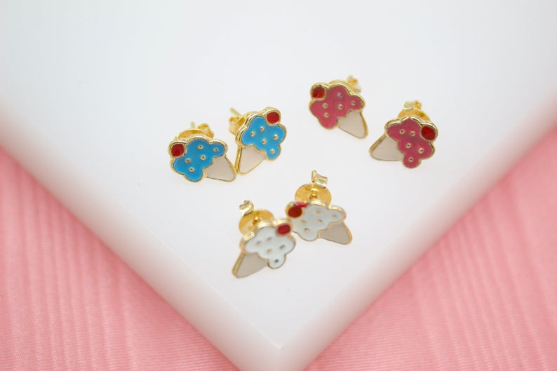 Three pairs of colorful enamel ice cream cone stud earrings rest on a white display surface against a pink background.