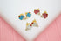 Three pairs of colorful enamel ice cream cone stud earrings rest on a white display surface against a pink background.