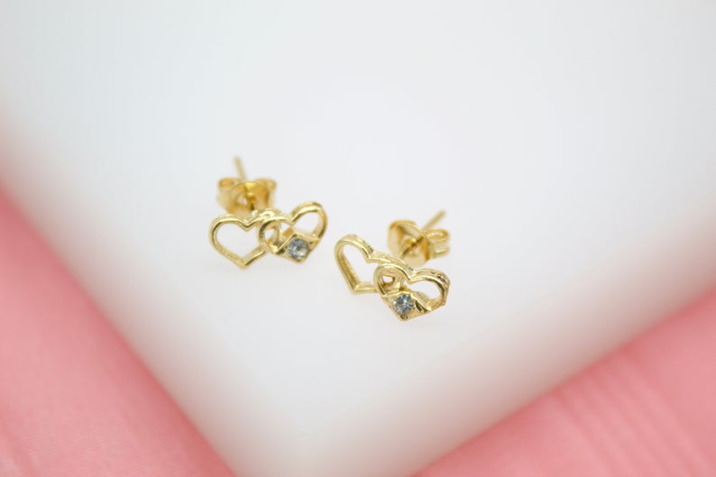 A pair of gold double heart stud earrings with sparkling cubic zirconia stones rests on a clean white surface.