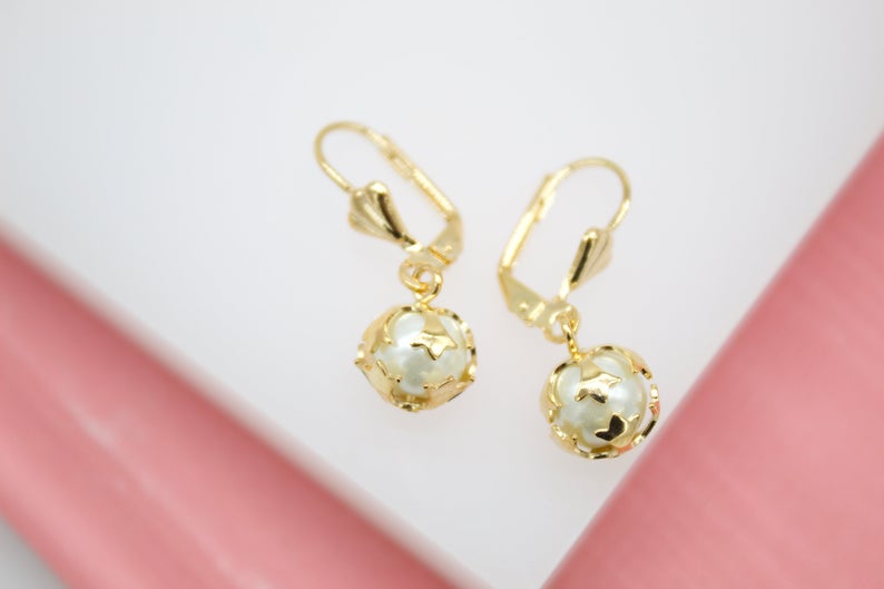 A pair of gold leverback earrings features dangling white pearl beads encased in delicate star-cutout cages.