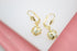 A pair of gold leverback earrings features dangling white pearl beads encased in delicate star-cutout cages.