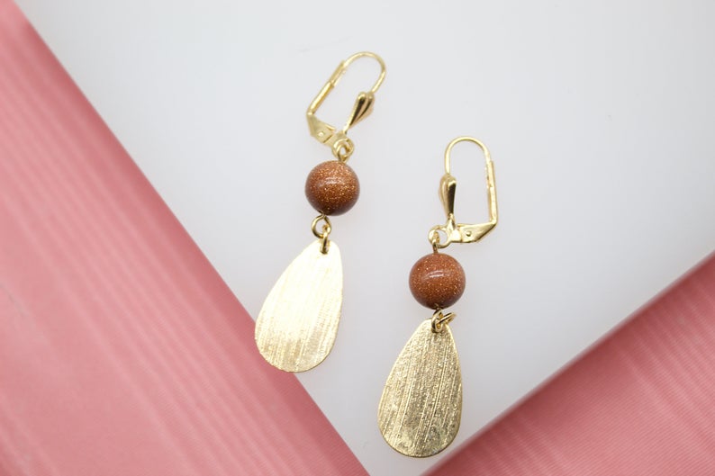 A pair of elegant gold leverback earrings features sparkling brown sandstone beads paired with brushed teardrop pendants.