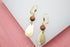A pair of elegant gold leverback earrings features sparkling brown sandstone beads paired with brushed teardrop pendants.