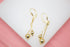 A pair of gold dangle earrings featuring delicate chains and polished sphere beads rests on a white display surface.