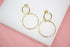A pair of elegant gold double hoop earrings embellished with sparkling cubic zirconia stones rests on a white display surface.