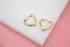 A pair of shiny gold heart-shaped hoop earrings rests on a white display surface against a soft pink background.