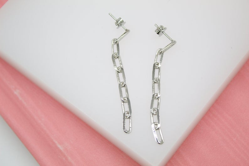 A pair of silver paperclip chain drop earrings rests flat against a white display surface.