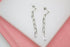 A pair of silver paperclip chain drop earrings rests flat against a white display surface.