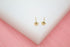 A pair of small gold star stud earrings rests on a white display against a pink background.