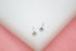 A pair of shiny silver star stud earrings rests on a white surface against a soft pink background.