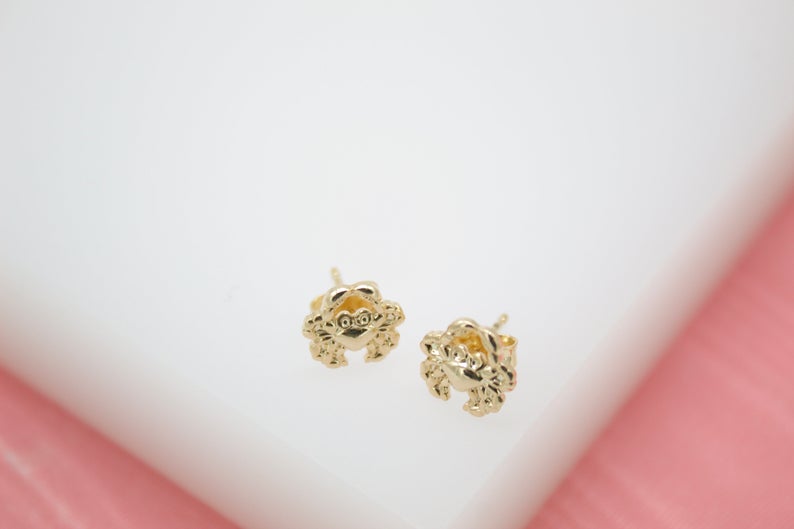 A pair of shiny gold crab stud earrings rests on a white display surface.