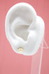 A white mannequin ear displays a shiny gold paw print stud earring against a pink background.