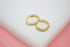 A pair of sparkling gold huggie hoop earrings rests delicately on a white and pink surface.