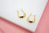 A pair of polished gold U-shaped hoop earrings rests on a white surface against a pink background.