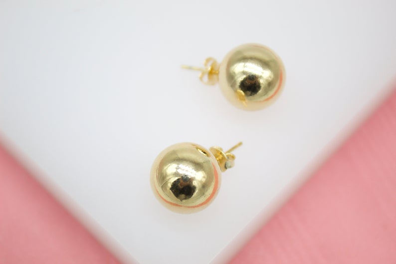 A pair of polished gold ball stud earrings rests against a white surface.