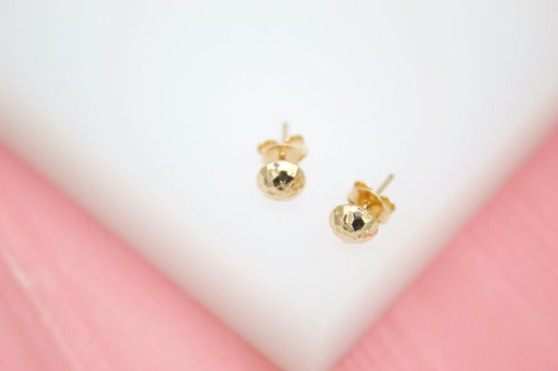 A pair of faceted gold ball stud earrings rests on a white and pink display surface.