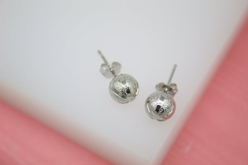A pair of textured silver ball stud earrings rests against a white and pink background.