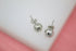 A pair of textured silver ball stud earrings rests against a white and pink background.