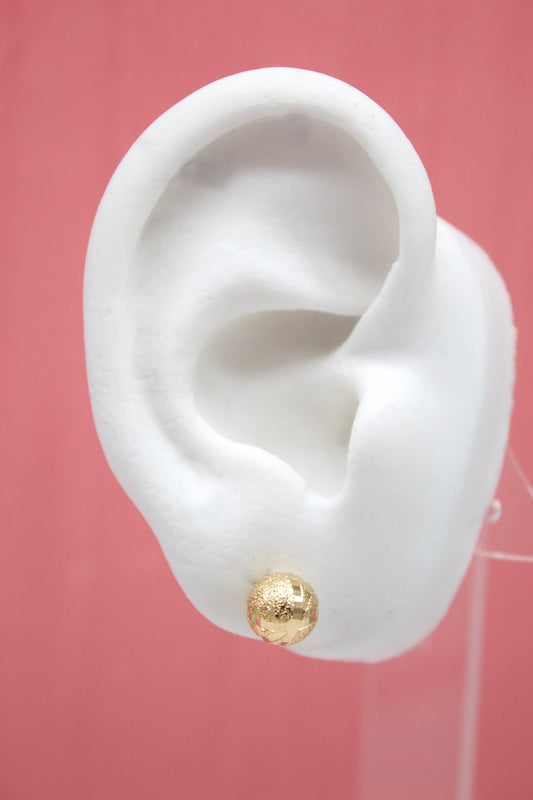 A white mannequin ear displays a textured gold ball stud earring against a pink background.