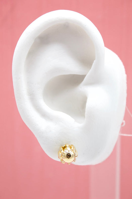 A white mannequin ear displays a delicate gold ladybug stud earring against a soft pink background.
