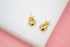 A pair of polished gold cage stud earrings rests on a white display surface.