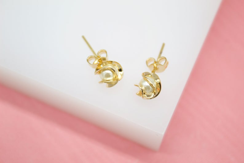 A pair of elegant gold stud earrings feature a delicate pearl nestled inside a swirling petal design.