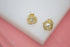 A pair of gold wire-wrapped stud earrings featuring lustrous white pearls rests on a white display block against a soft pink background.