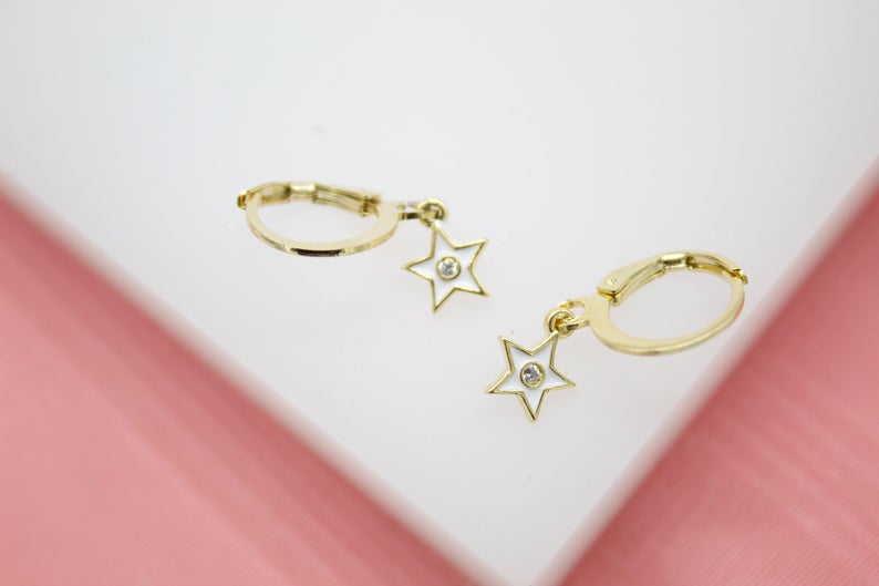 A pair of gold huggie hoop earrings features dangling white enamel star charms set with sparkling cubic zirconia stones.
