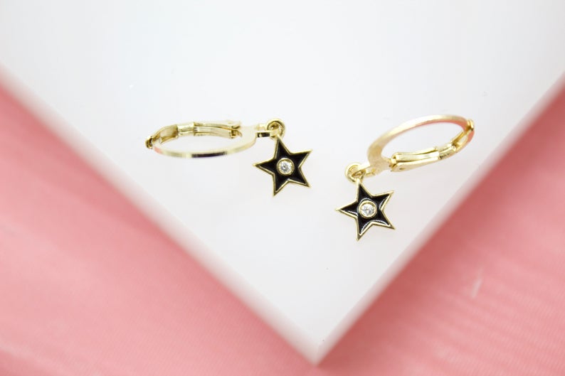 A pair of gold huggie hoop earrings features hanging black star charms accented with central diamonds.