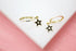 A pair of gold huggie hoop earrings features hanging black star charms accented with central diamonds.