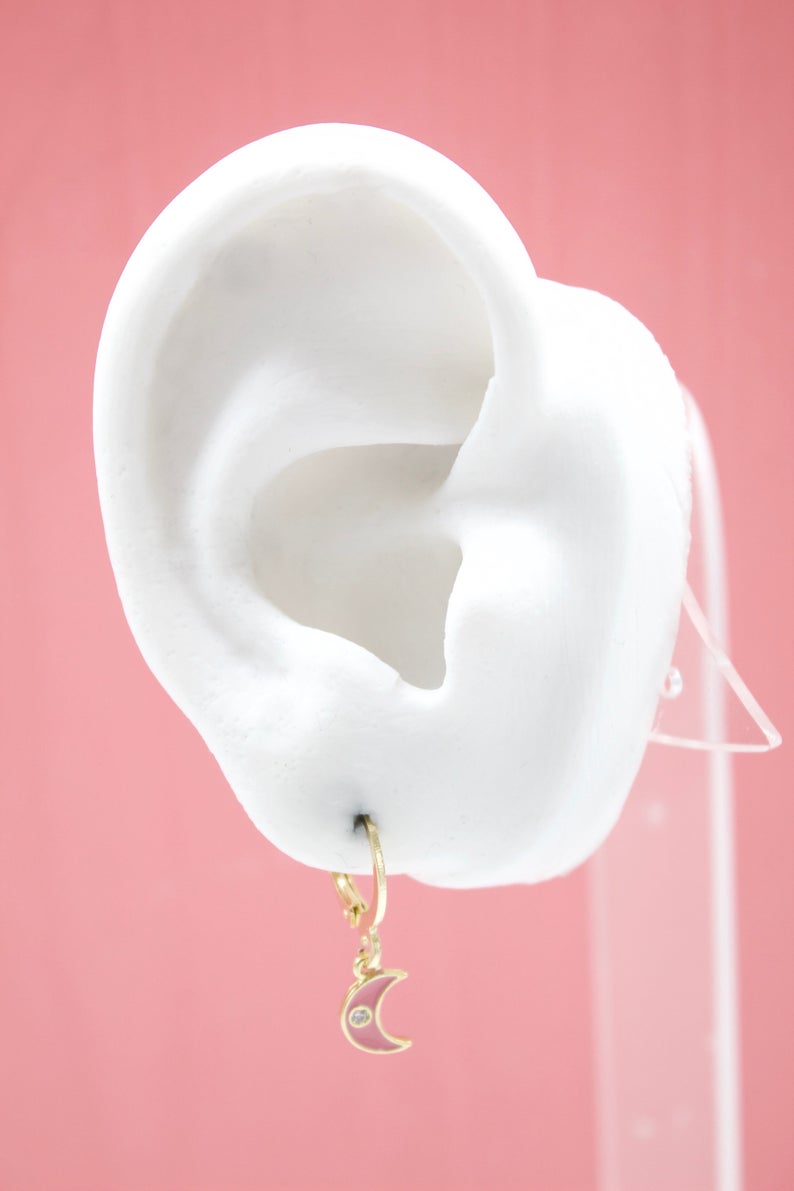 A white display ear showcases a gold hoop earring with a pink crescent moon pendant featuring a small diamond accent.