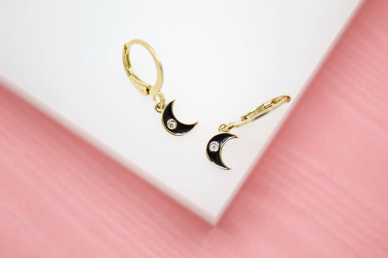 A pair of gold huggie hoop earrings features dangling black enamel crescent moon charms accented with sparkling crystals.