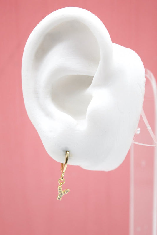 A white mannequin ear displays a gold huggie hoop earring featuring a sparkly initial Y charm.