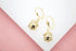 Two gold dangle earrings featuring decorative sphere charms rest on a white and pink display surface.