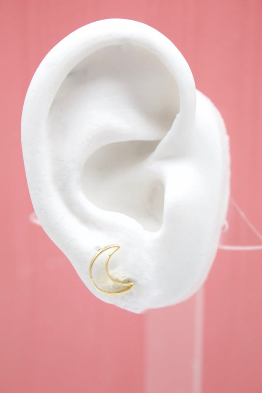 A white mannequin ear displays a delicate gold crescent moon stud earring against a pink background.