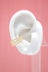 A white ear model displays a triple gold bead ear cuff against a pink background.