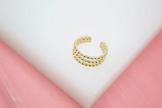 A gold-plated multi-row beaded ear cuff rests on a white display surface.