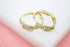 A pair of gold hoop earrings features a sparkling pave buckle design resting on a white display surface.
