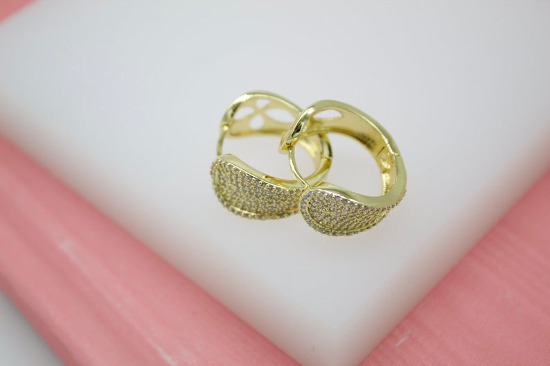 A pair of elegant gold hoop earrings embellished with sparkling cubic zirconia stones rests on a white display stand.