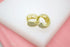 A pair of sparkling gold huggie hoop earrings encrusted with tiny cubic zirconia stones rests against a soft white and pink background.