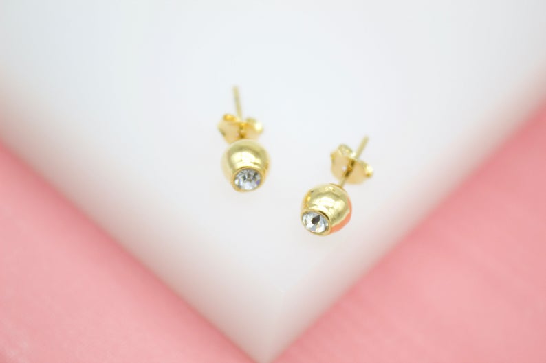 A pair of gold ball stud earrings featuring sparkling inset crystals rests on a light background.