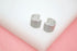 A pair of silver pave huggie hoop earrings rests on a white and pink display surface.