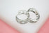 Two silver hoop earrings rest on a white surface, showcasing intricate cut-out patterns and sparkling crystal embellishments.