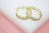 A pair of gold hoop earrings embellished with sparkling cubic zirconia crystals rests on a white and pink surface.