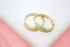 A pair of pave-set diamond gold hoop earrings rests on a white display surface against a pink background.